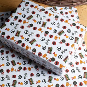May include: White wrapping paper with a racing theme. The paper is covered in colorful illustrations of racing helmets, steering wheels, checkered flags, trophies, and medals. The paper is wrapped around a gift.
