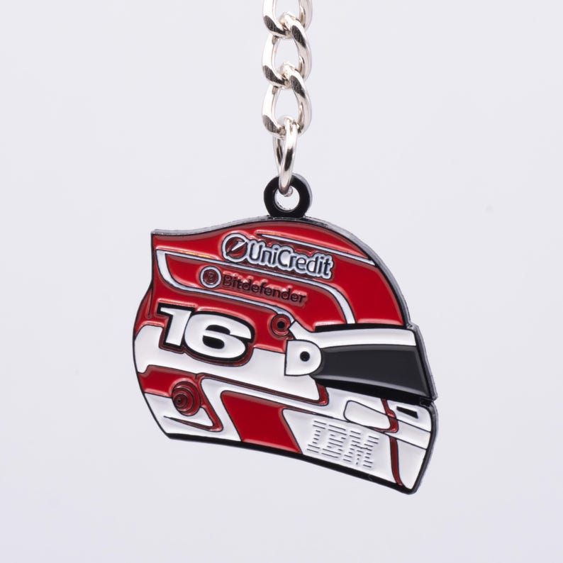 May include: A red, white, and black helmet-shaped keychain with the number 16. The keychain has a silver chain and a black ring. The helmet design includes the UniCredit and Bitdefender logos.