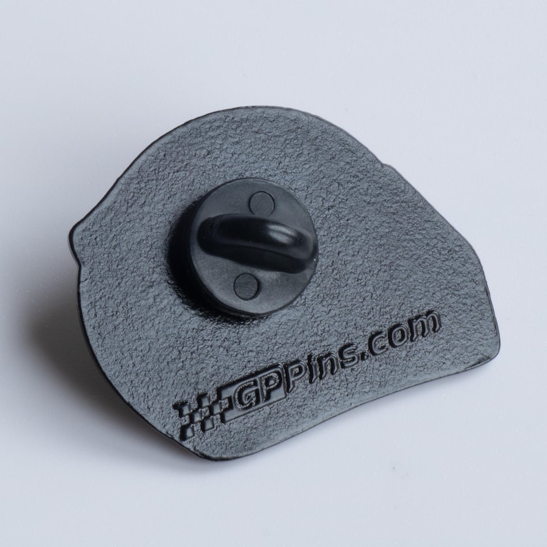May include: Black enamel pin with a racing helmet design. The back of the pin has a black metal clasp and the text "GPPins.com" with a checkered flag design.