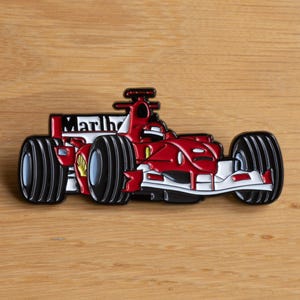 May include: A red and black enamel pin of a Formula 1 race car with the word "Marlboro" on the side.