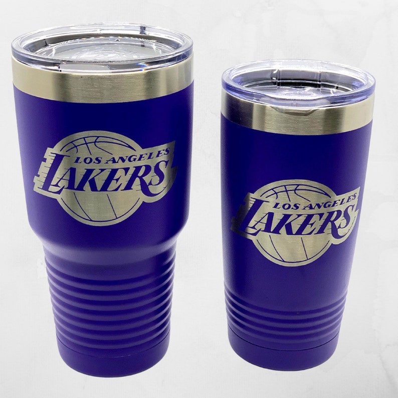 May include: Two purple insulated tumblers with the Los Angeles Lakers logo in gold. The tumblers have a silver rim and clear lid. One is a 30 oz tumbler, the other is a 20 oz tumbler.