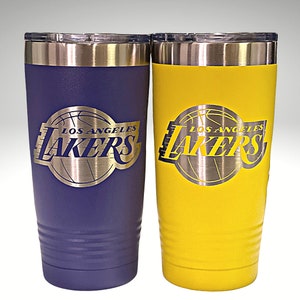 May include: Two insulated tumblers, one purple and one yellow, featuring the Los Angeles Lakers logo. The logo is a silver-colored emblem with the team name and a basketball design. Both tumblers have a silver rim and lid.