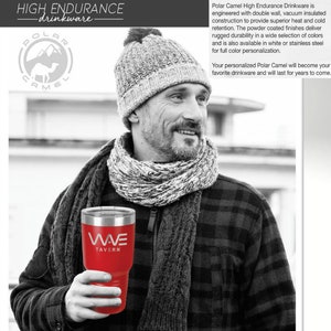 May include: A red Polar Camel tumbler with the text "WAVE TAVERN" is held by a person. The tumbler is stainless steel and has a silver rim. The person is wearing a gray knit hat, a scarf, and a plaid shirt. The image also includes the Polar Camel logo.
