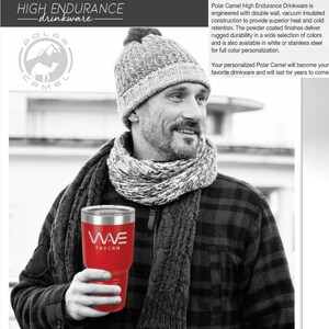 Puede incluir: Un vaso rojo de acero inoxidable con un logotipo en blanco y negro que dice "WAVE TAVERN". El vaso lo sostiene una persona que lleva una camisa a cuadros en blanco y negro y una bufanda gris.