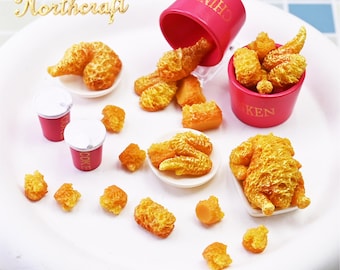 May include: Miniature food set featuring fried chicken, chicken drumsticks, and small cups of soda. The food items are arranged on a white plate, with a pink bucket of chicken and a spilled container. The word "Northcraft" is in gold script.