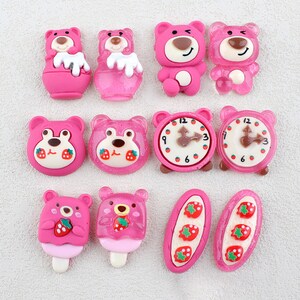 May include: Pink resin flatback embellishments with various designs including bears, clocks, and strawberries.