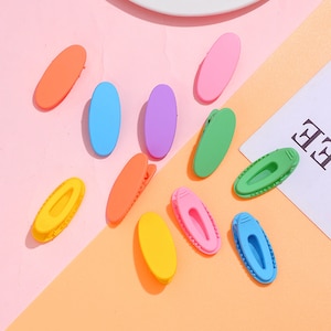 Peut inclure: Assortiment de dix pinces à cheveux ovales en plastique de différentes couleurs, dont rose, bleu, vert, jaune et orange.
