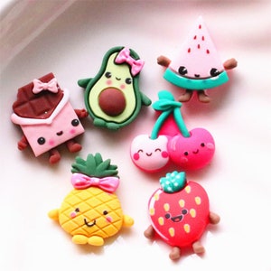 Pode incluir: Um conjunto de sete amuletos coloridos de frutas e chocolate de desenho animado com rostos fofinhos. Os amuletos são feitos de um material macio e flexível e são perfeitos para adicionar um toque de fantasia a artesanatos, joias ou outros projetos.