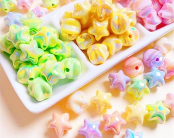 May include: Assortment of iridescent star-shaped beads in various pastel colors, including pink, yellow, green, and blue. The beads are arranged in three separate compartments on a white plate.