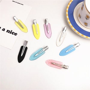 May include: Eight hair clips with different colored plastic tops. The clips are silver and have a small tooth on the end. The plastic tops are black, yellow, pink, light blue, dark blue, white, and two shades of pink.