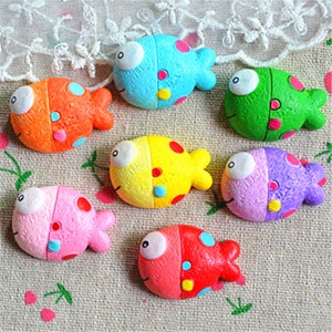 May include: Seven colorful fish-shaped magnets with polka dots and googly eyes. The magnets are made of resin and are approximately 2 inches long.