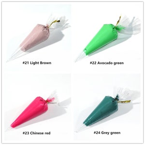 May include: Four plastic piping bags filled with different coloured frosting. The bags are labelled with numbers and colours: #21 Light Brown, #22 Avocado green, #23 Chinese red, and #24 Grey green.