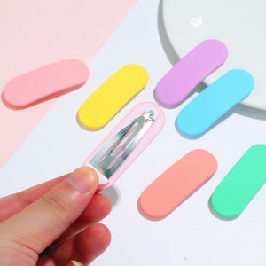 Peut inclure: Assortiment de pinces à cheveux en plastique de différentes couleurs. Les pinces sont de forme ovale et sont disponibles en rose, jaune, bleu clair, lavande et corail. Une pince a un ressort en métal argenté.