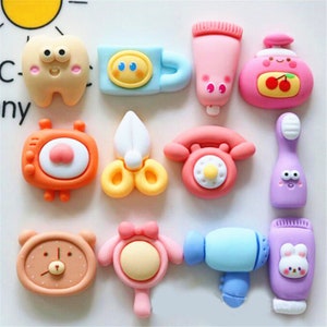 May include: A set of 10 colorful, cartoon-style resin charms featuring various objects like a tooth, a cup, a tube of toothpaste, a bottle of soap, a radio, scissors, a telephone, a toothbrush, a mirror, and a hairdryer.