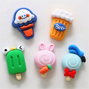 May include: Six colorful fridge magnets shaped like different treats, including an ice cream cone, a beer mug, a popsicle, a lollipop, and two swirl lollipops.