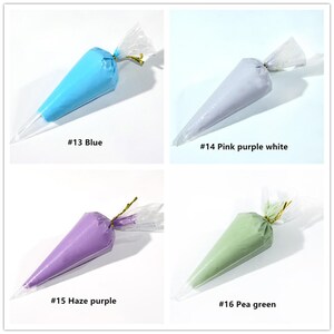 May include: Four plastic piping bags filled with different coloured frosting. The bags are tied off with gold string. The colours are blue, light purple, purple, and green. The bags are labelled with numbers and colour names: #13 Blue, #14 Pink purple white, #15 Haze purple, #16 Pea green.