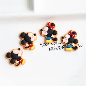 May include: Four cartoon character embellishments featuring Mickey Mouse and Minnie Mouse. The characters are in various poses, including blowing a kiss and holding hands. The embellishments are made of plastic and have a glossy finish. They are perfect for adding a touch of Disney magic to your crafts.