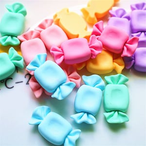 May include: A selection of colourful, wrapped candy-shaped decorations. The sweets are in various pastel shades, including pink, blue, green, yellow, and purple. The image is a close-up shot, highlighting the details of the candy shapes.