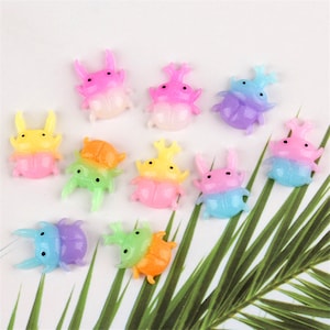 May include: Assortment of ten colourful, iridescent, resin beetle charms. Each beetle charm is approximately 1 inch in size and features a two-toned colour scheme. The colours include yellow, orange, green, blue, pink, and purple.