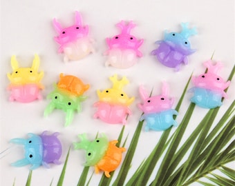May include: Assortment of ten colourful, iridescent, resin beetle charms. Each beetle charm is approximately 1 inch in size and features a two-toned colour scheme. The colours include yellow, orange, green, blue, pink, and purple.