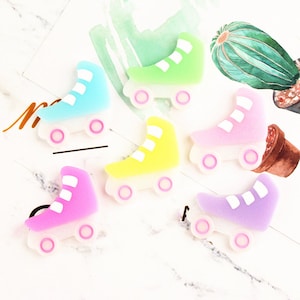 May include: Six colourful roller skate charms in various pastel colours, including light blue, green, yellow, pink, and purple. Each charm features a white stripe design and pink wheels.