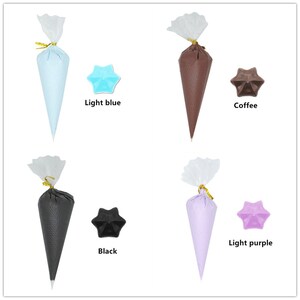 May include: Four disposable piping bags filled with different coloured frosting. The colours are light blue, coffee, black, and light purple. Each bag is tied with a gold ribbon and has a clear plastic cover.