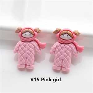 May include: Two pink plastic girl figurines wearing pink quilted snowsuits with brown hair and brown eyes. The figurines are wearing pink hats and scarves. #15 Pink girl