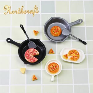 Op de afbeelding: Miniatuur pizza- en kookgerei set. De set bevat een zwarte koekenpan met een pizzapunt, een grijze koekenpan met een hele pizza, een wit bord met pizzapunten en een kleine witte pan met een pizza. Ook inbegrepen zijn een spatel en pizzapunten.