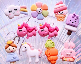 May include: Assortment of colourful resin flatback embellishments featuring a unicorn, a flower, a cloud with a rainbow, a princess, a bunny, a carrot, an ice cream cone, and a popsicle.