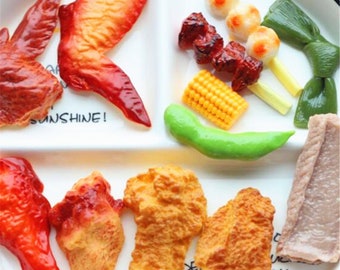 May include: A collection of miniature food items, including chicken wings, fried chicken, corn on the cob, a green bean, and a skewer of meat and vegetables. The food items are made of plastic and are designed to look realistic.