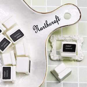 May include: White miniature computer-shaped charms with black screens and a white frame. The charms are arranged on a white serving dish with gold trim. The word "Northcraft" is written in cursive on the dish.