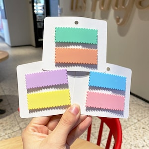 May include: Set of six colorful hair clips with scalloped edges. The clips are in shades of green, orange, purple, blue, and pink.