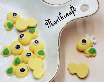 May include: A collection of yellow and green turtle-shaped resin embellishments with black eyes. The embellishments are on a white ceramic plate with a gold rim. The word "Northeraft" is written in black on the plate.