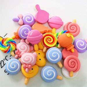 Può includere: Una collezione di ciondoli colorati a tema caramelle, tra cui lecca-lecca, bastoncini di zucchero e gommose. I ciondoli sono realizzati in pasta polimerica e sono perfetti per aggiungere un tocco di dolcezza ai tuoi lavoretti.