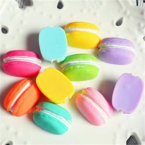 May include: Assortment of colourful macarons with white filling. The macarons are arranged on a white surface.