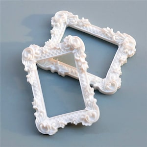 Può includere: Due cornici per foto bianche ornate con un design decorativo. Le cornici sono in plastica e sono perfette per aggiungere un tocco di eleganza a qualsiasi arredamento domestico.