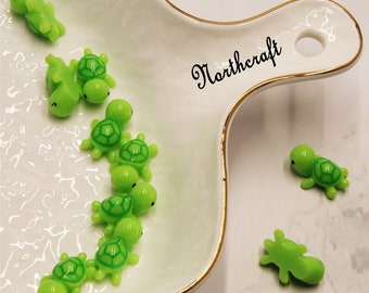 May include: A collection of small green turtle figurines on a white plate with a gold rim. The plate has the word "Northcraft" written on it in black cursive.