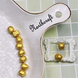 May include: A collection of small, gold-colored pig figurines arranged on a white serving platter with gold trim. The platter has the word "Northcraft" in black script. Two pig figurines are displayed in a white frame.