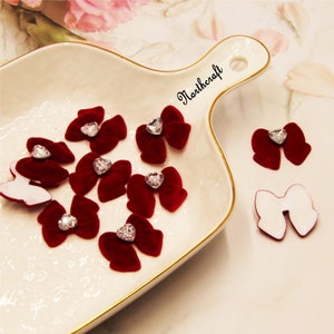 Op de afbeelding: Een verzameling van tien rode fluwelen strikken met heldere strass steentjes in het midden. De strikken zijn gerangschikt op een wit bord met een gouden rand. De tekst "Northercraft" is op het bord gedrukt.