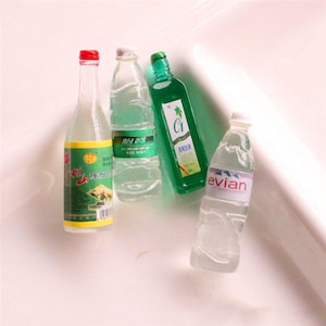 Op de afbeelding: Vier miniatuurflesjes met verschillende dranken. Een helder flesje met een groen etiket en de tekst "Evian" erop. Een helder flesje met een groen etiket en Chinese tekst. Een helder flesje met een groen etiket en de tekst "C1" erop. Een helder flesje met een groen etiket en Chinese tekst.