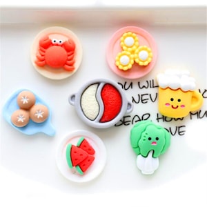 May include: A set of 10 colourful, cartoon-style food charms. The charms include a crab, a bowl of soup, a plate of watermelon, a plate of dumplings, a plate of corn, a glass of beer, and a broccoli.