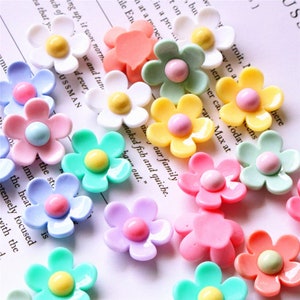 May include: Assortment of colourful daisy-shaped resin embellishments with a raised centre. The embellishments are in various colours, including pink, yellow, blue, green, and white.