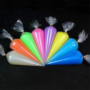 Puede incluir: Ocho bolsas de slime de colores en varios colores, incluyendo rosa, morado, amarillo, azul, verde y naranja. Las bolsas son de plástico transparente y están atadas con una cinta dorada.