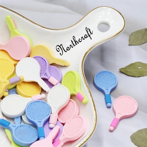 May include: A white ceramic dish with a gold rim, containing a variety of colorful miniature tennis rackets. The dish has the word "Northcraft" written on it in black.