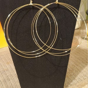 May include: Gold hoop earrings with multiple layers of wire. The earrings are displayed on a black jewelry stand.