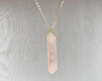 May include: A gold chain necklace with a rose quartz pendant. The pendant is a long, pointed crystal.