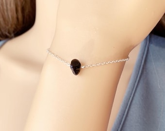 Peut inclure: Un bracelet délicat en chaîne argent avec un seul charme en pierre noire.