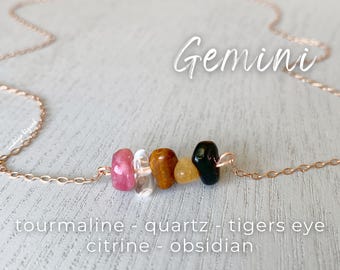 May include: A rose gold chain necklace with a charm featuring five gemstone beads: pink tourmaline, clear quartz, brown tiger's eye, yellow citrine, and black obsidian. The charm is labelled "Gemini".