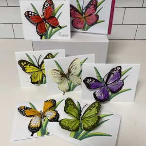 May include: Set of six blank greeting cards featuring colorful butterfly illustrations. Each card has a different butterfly design with a green grass background. The cards are perfect for sending a special message to someone you care about.