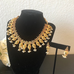 May include: A gold necklace and earrings set with a paisley design. The necklace features green and red stones and white pearls. The earrings are similar in design to the necklace.